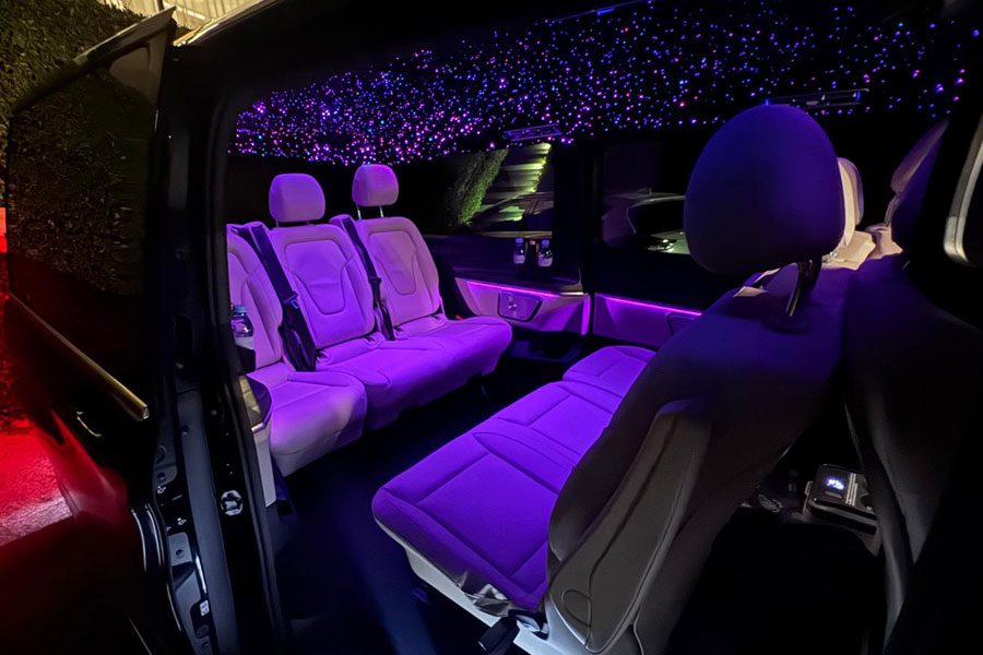 Intérieur personnalisé d'un véhicule de luxe avec plafond ciel étoilé LED et éclairage violet.